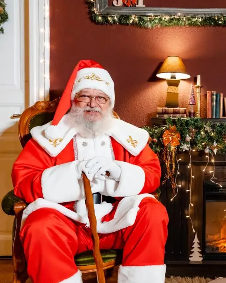 Moș Crăciun într-o cameră decorată de Crăciun, lângă șemineu